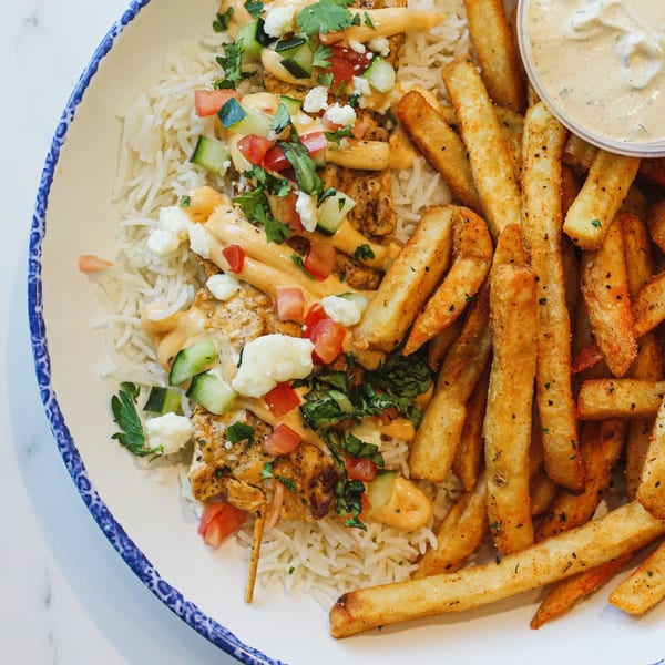 Tazā's Mediterranean chicken skewer with rice, fries, and a side of sauce.