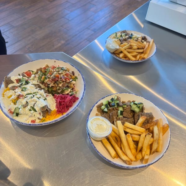 Three Mediterranean dishes on a metal counter, including a large bowl with meat, rice, and vegetables.