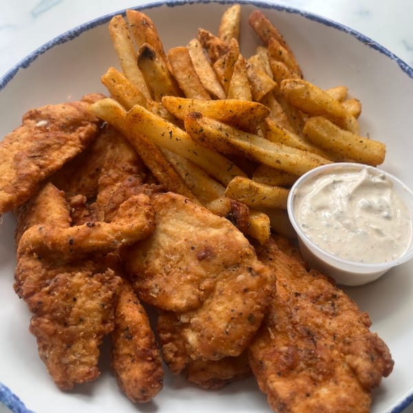Crispy chicken tenders and seasoned french fries with a side of dipping sauce in a white bowl.