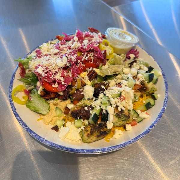 A vibrant Mediterranean salad with feta, pickled cabbage, hummus, and grilled vegetables on a white plate.