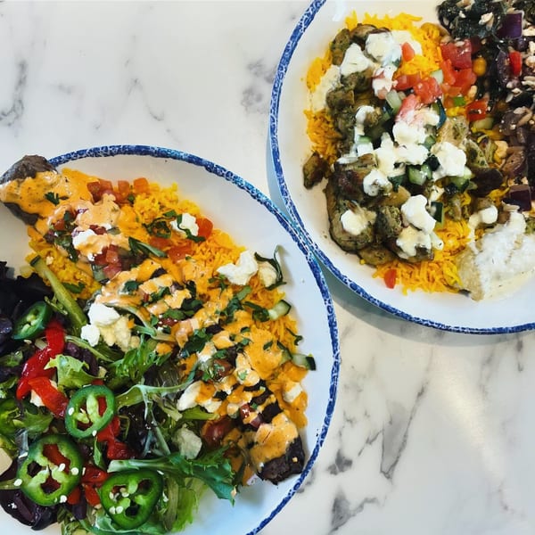 Two vibrant Mediterranean bowls with rice, meat, fresh vegetables, and sauces on a marble surface.