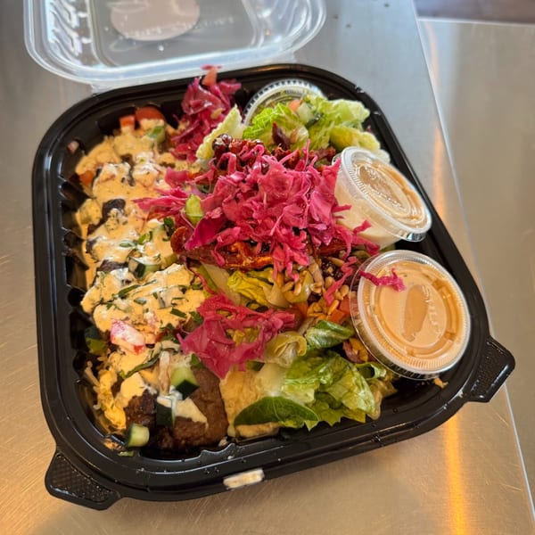 Tazā Mediterranean bowl with meat, salad, pickled cabbage, and two sauce containers in a takeout box.