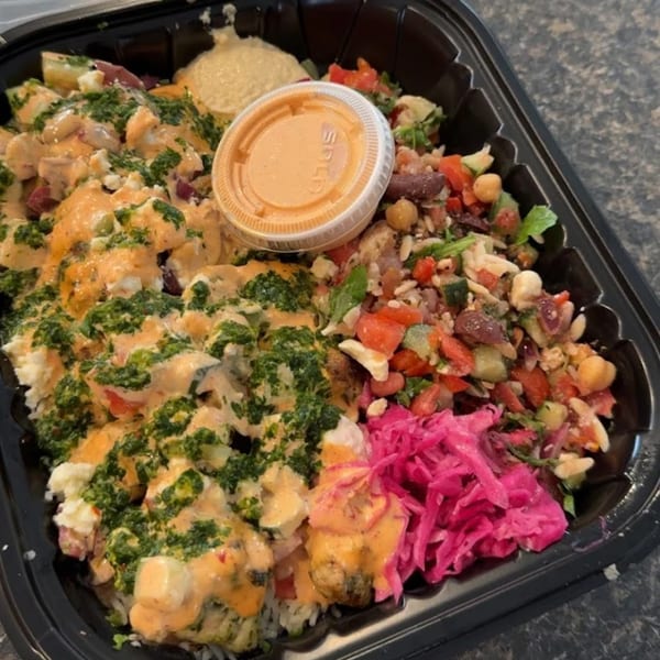 Tazā Mediterranean bowl with chicken, rice, salad, hummus, pickled cabbage, and sauces in a black container.