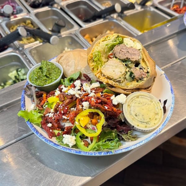 Tazā Mediterranean wrap and salad with pesto and dressing on a blue-rimmed plate.