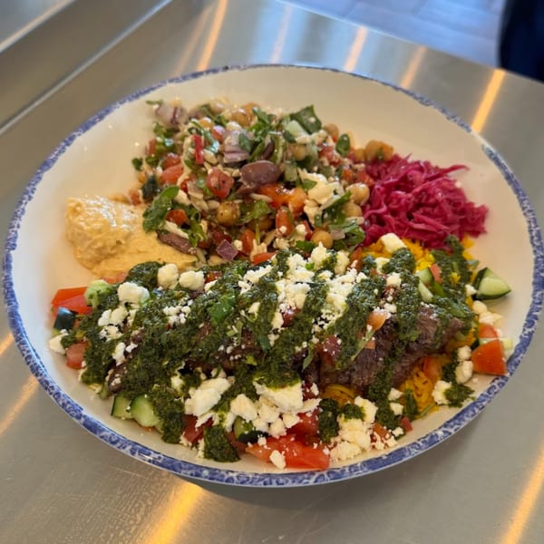A Tazā Mediterranean bowl with hummus, chickpea salad, pickled cabbage, and meat with pesto and feta.